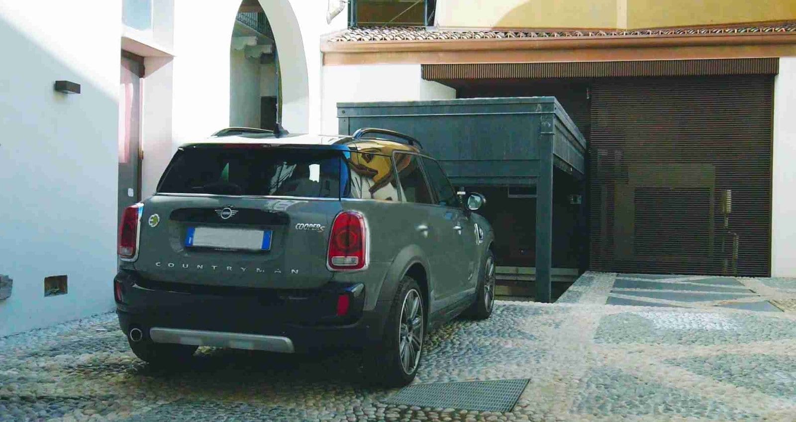 Auto verde parcheggiata davanti a struttura metallica verde, cortile con edifici residenziali sullo sfondo
